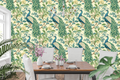 Chinoiserie peacock wallpaper featuring magnificent peacock birds with detailed emerald and sapphire plumage, cascading golden-eyed tail feathers, blue and ivory botanical blossoms, trailing branches, and rich green foliage on a warm ivory ground — premium heritage bird wallpaper by WallpaperPixi