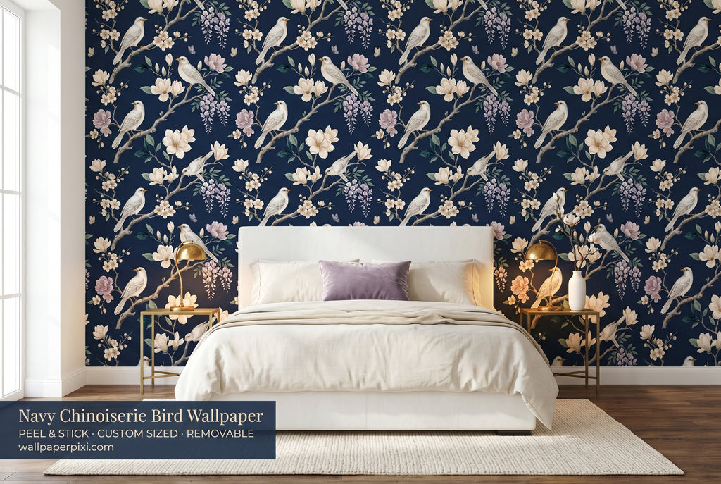 Navy chinoiserie bird and magnolia wallpaper in a bright dramatic bedroom with a white upholstered bed cream bedding brass accents and warm candlelight