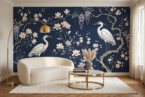 Luxury chinoiserie wallpaper mural featuring two white herons among magnolia blossoms, cherry blossom branches, and wisteria on a deep navy blue background — premium botanical bird wall art by WallpaperPixi
