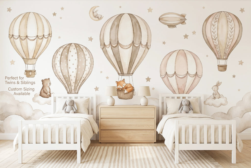 Hot air balloon nursery wallpaper mural in a gender neutral twin toddler room with two cribs and soft neutral decor