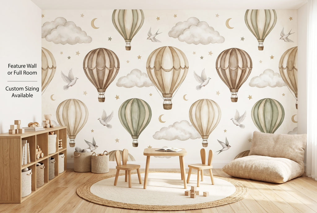 Neutral hot air balloon wall mural spanning the full back wall of a gender-neutral playroom as a wide panoramic scene — beige, taupe and sage balloons with white doves and gold crescent moons above wooden toy shelves, a round cream rug and small wooden play table.