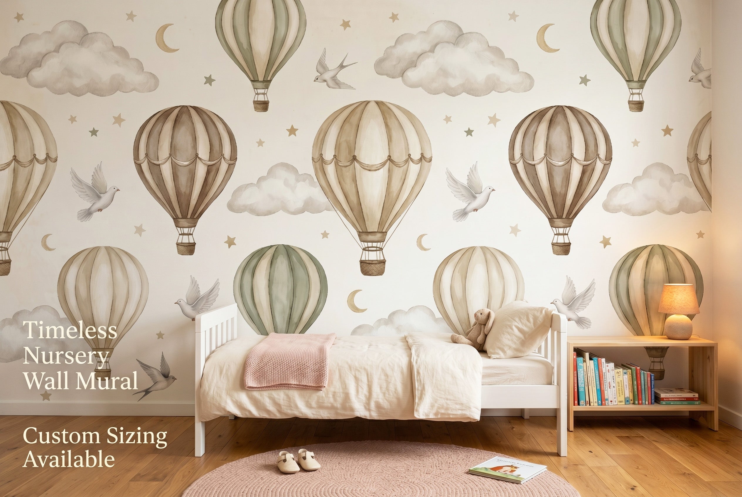 Warm neutral hot air balloon wall mural spanning the full feature wall of a cosy toddler girl's bedroom — the panoramic beige and sage sky scene with white doves and gold moons above a low white toddler bed with cream linen and a blush knitted blanket.