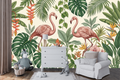 Tropical flamingo wallpaper mural featuring a pair of elegant pink flamingos among lush monstera fronds, banana leaves, palm fronds, red heliconia flowers, golden Bird of Paradise blooms, and soft pink orchids on warm ivory ground — premium tropical botanical wall mural by WallpaperPixi